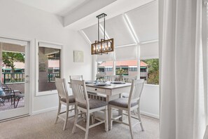A dining area with a white table, four chairs, and a hanging light fixture. - Shelter Cove 2BR villa with lagoon views, Community Pool, Sleeps 8! (Hilton Head Island)