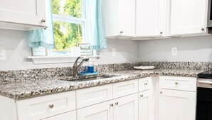 Una cucina con mobili bianchi, un piano di lavoro in granito, una finestra vista verde e un tappeto decorativo sul pavimento.