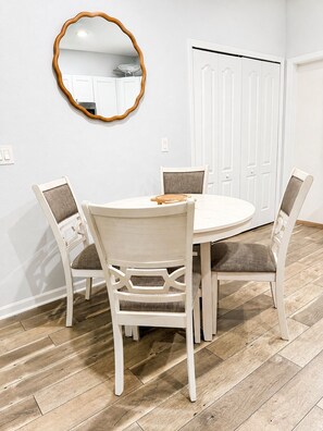 A dining area with a round table, four chairs, a wooden-framed mirror, and a white door in the background. - NEW!!! Cozy 2-bedroom house minutes to historic downtown St. Augustine & ocean. (St. Augustine)