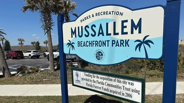 Segnale per il parco balneare di Mussallem, con palme e un parcheggio sullo sfondo.