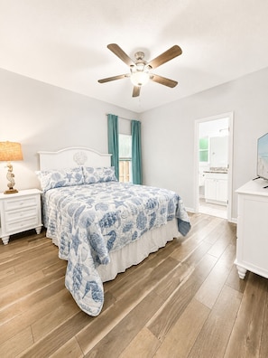 A bedroom with a bed, a nightstand, a ceiling fan, a window with curtains, and a door leading to another room. - NEW!!! Cozy 2-bedroom house minutes to historic downtown St. Augustine & ocean. (St. Augustine)