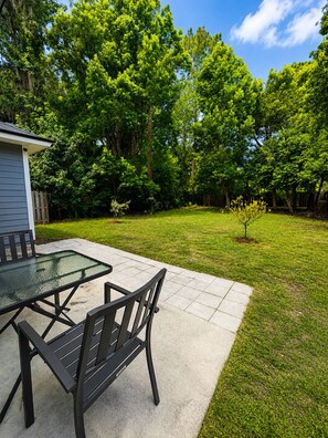 A patio with a glass-top table and chairs, surrounded by a well-maintained lawn and trees. - NEW!!! Cozy 2-bedroom house minutes to historic downtown St. Augustine & ocean. (St. Augustine)