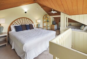 A bedroom with a large bed, a wooden headboard, a nightstand with a lamp, a bookshelf, and a television. - Walk to Poipu Beach | Garden Condo | AC, Pools, Hot Tub & Tennis (Koloa)