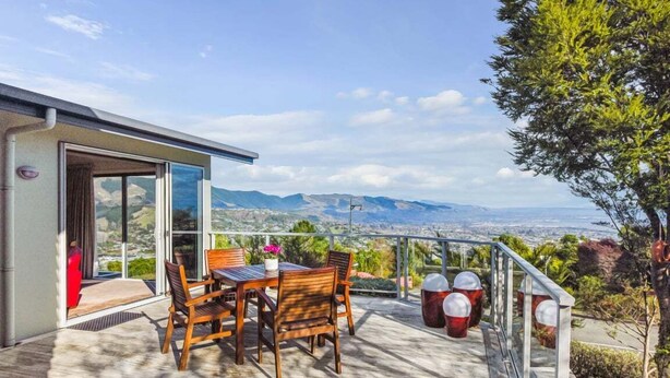 Eine Terrasse mit Tisch und Stühlen, eine Glastür, die zu einer Holzterrasse führt, und eine Aussicht auf Berge.