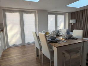 A modern dining area with a wooden table, white chairs, and a skylight above.