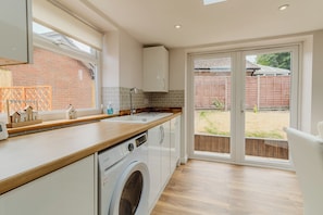 A modern kitchen with a built-in washing machine, wooden countertops, and a large sliding glass door leading to a backyard.