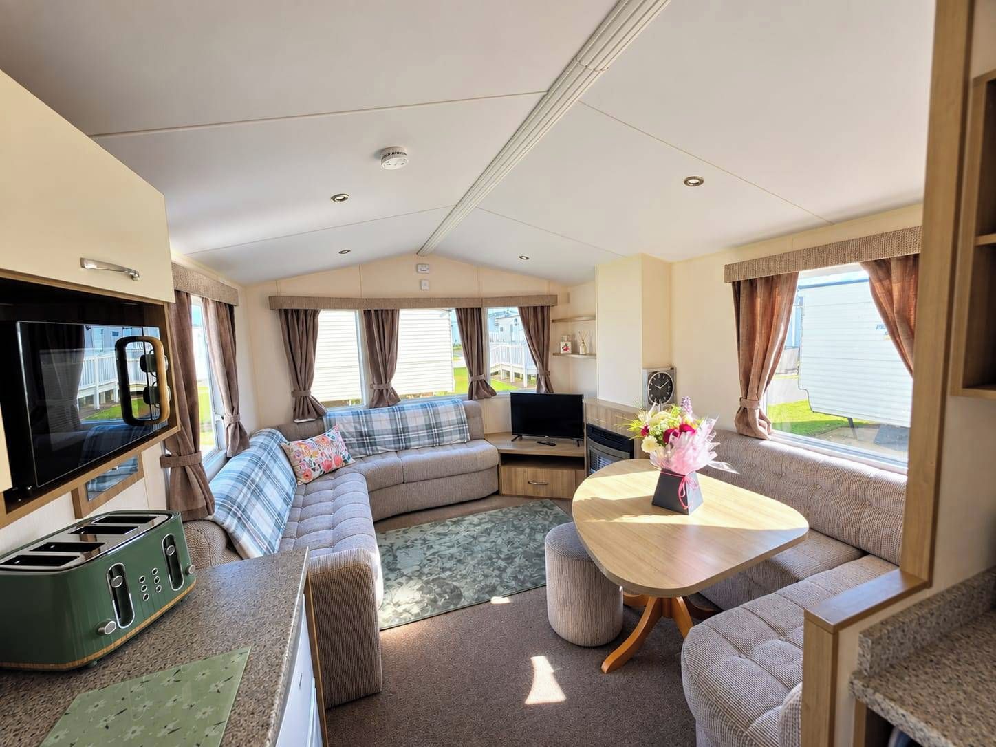 A caravan interior with a sofa, television, table, and a kitchenette area.