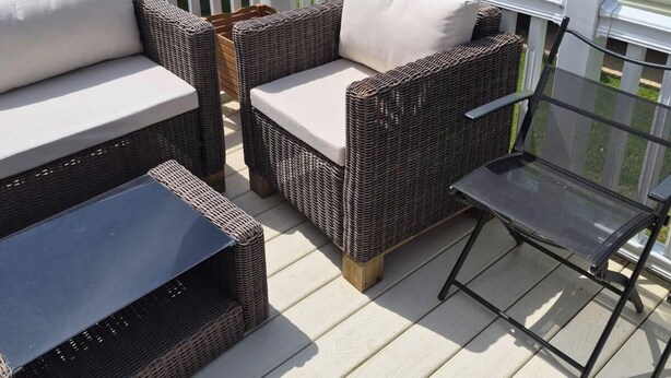 Eine Terrasse mit Korbmöbeln und einem Glastisch, umgeben von Wohnmobilen.