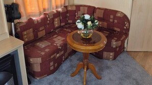 Ein gemütlicher Wohnbereich mit einer Couch, einem kleinen Tisch mit Blumenvase, einem Heizgerät und einer Steckdose an der Wand.