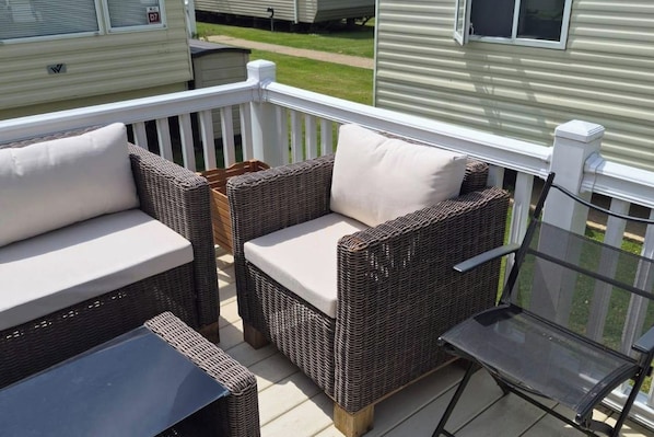A deck with wicker furniture and a glass table.