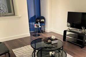 Un salon moderne avec une table basse en verre, un canapé noir, un meuble pour la télévision et une porte bleue.