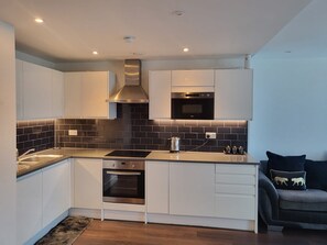 A modern kitchen with white cabinets, a black tiled backsplash, stainless steel appliances, and a built-in oven. - Cozy London Apartment with 2 Bedrooms (London)