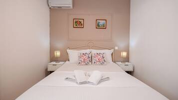 A neatly made bed with floral pillows, two bedside lamps, and a wall-mounted air conditioner.
