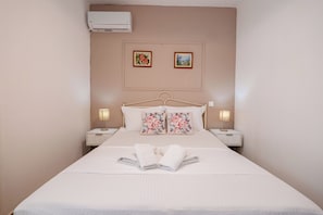 A neatly made bed with floral pillows, two bedside lamps, and a wall-mounted air conditioner. - Corfu Dream Holidays Villas (Corfu)