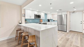 Una cocina moderna con armarios blancos, una isla grande con taburetes, electrodomésticos de acero inoxidable y un salpicadero de azulejos azules.