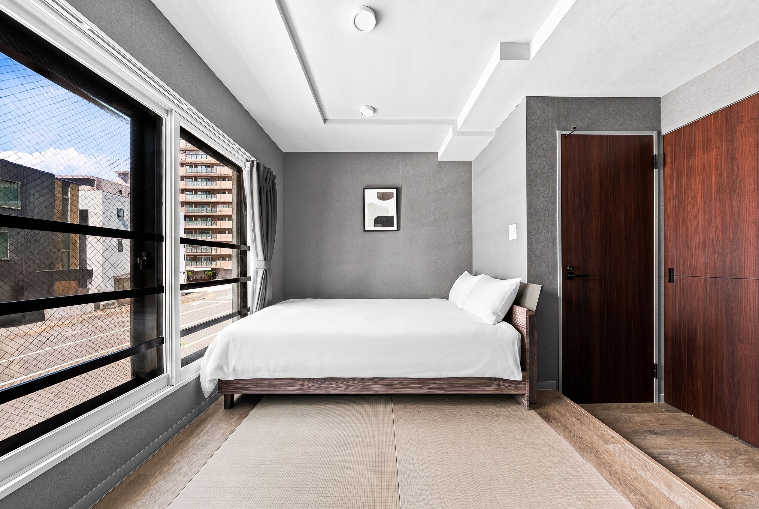 A modern bedroom with a large window, a bed, a door, and a framed picture on the wall.