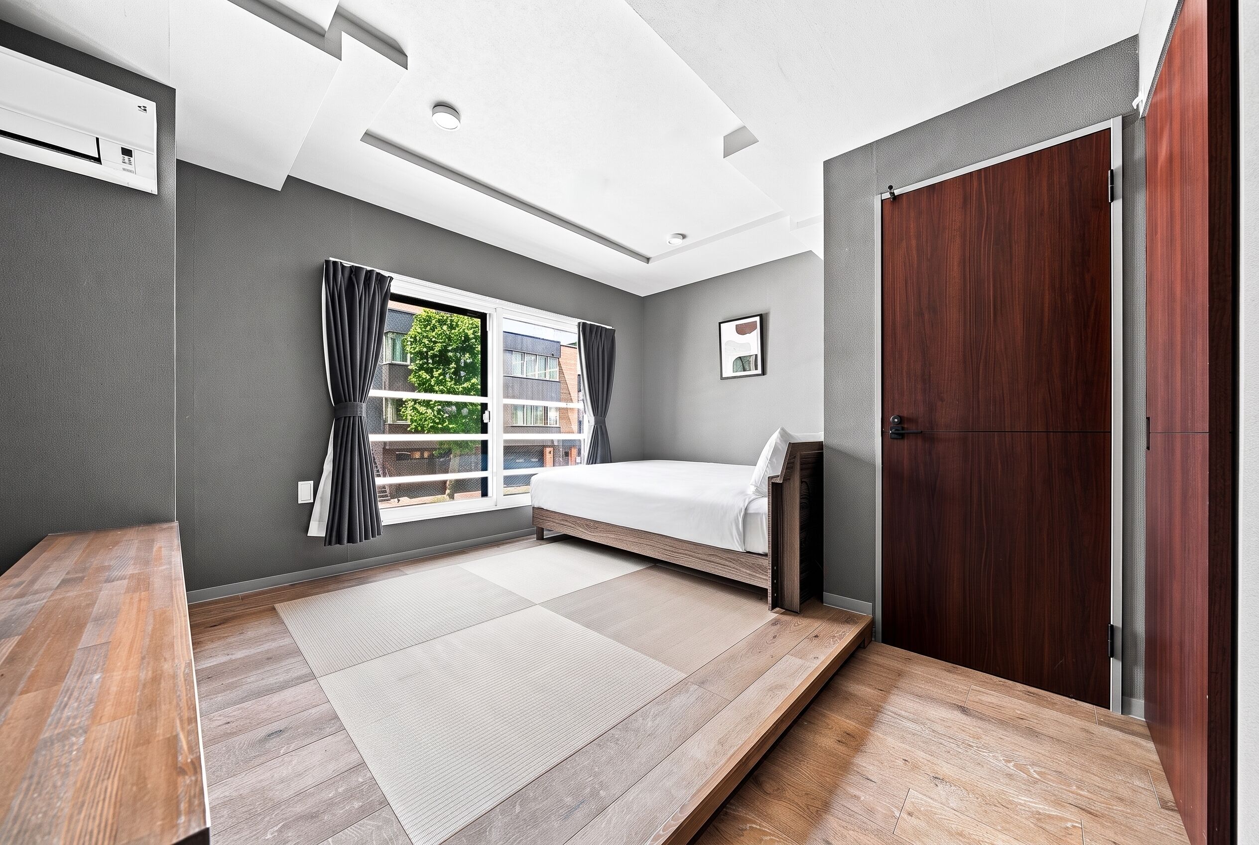 A modern bedroom with a bed, a wooden desk, a window with curtains, and a door.