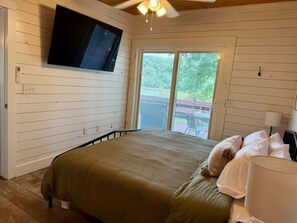 Quarto com cama, TV fixada na parede e porta de vidro deslizante para área externa.