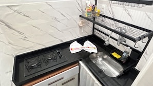 Una cocina con encimera de mármol, un fregadero, una estufa y una alacena negra con utensilios de cocina.