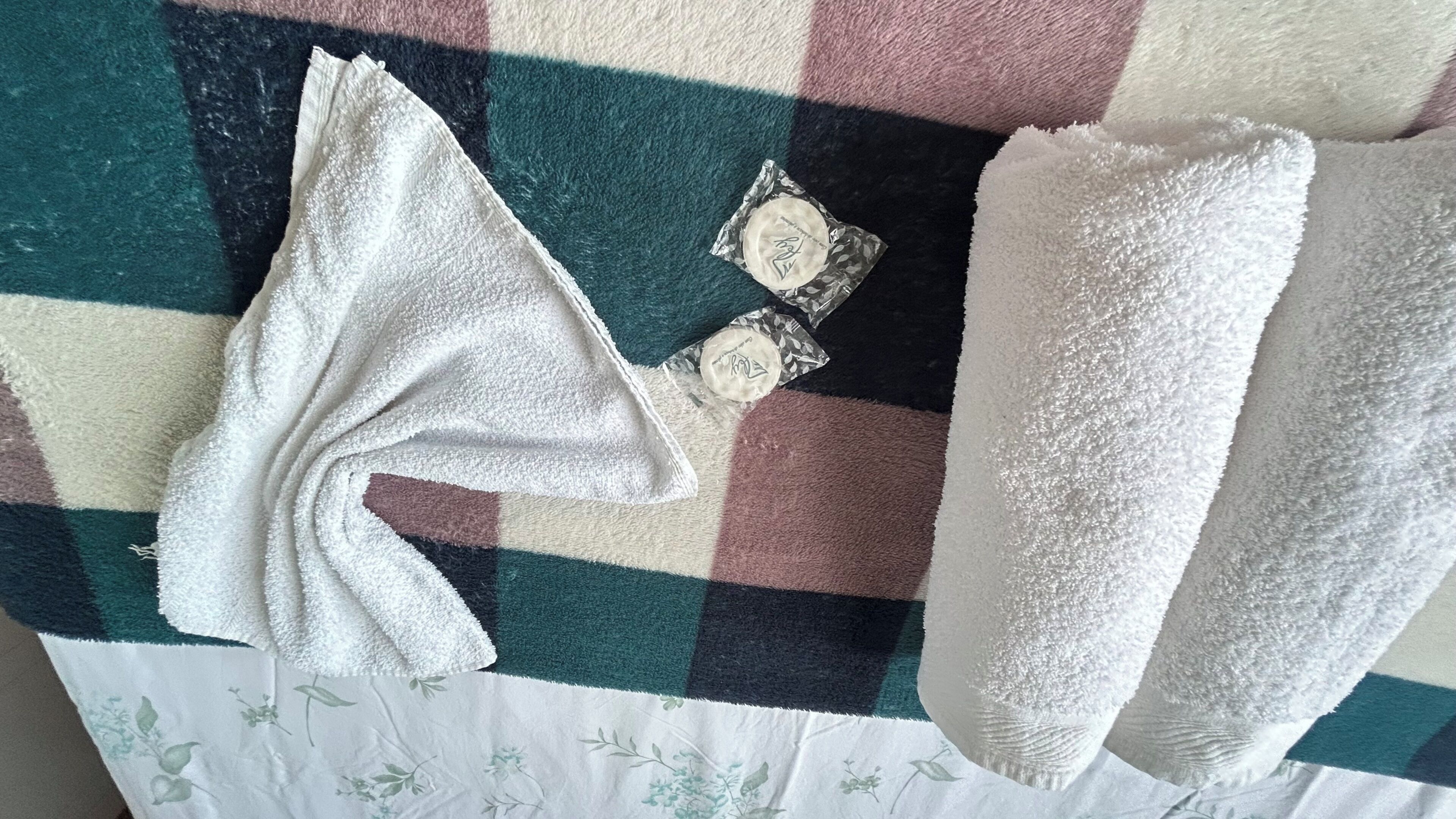 Una colcha a cuadros con una toalla blanca y dos objetos pequeños de color blanco encima.