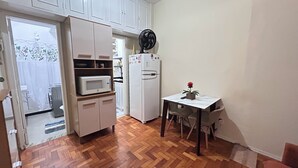 Una cocina compacta con microondas, refrigerador y una pequeña mesa con una planta en maceta.