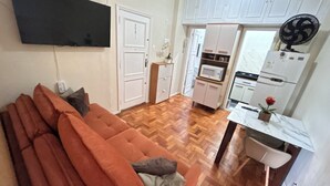 Un espacio habitable compacto con sofá, televisor de pantalla plana, y cocina equipada con microondas, horno y refrigerador.