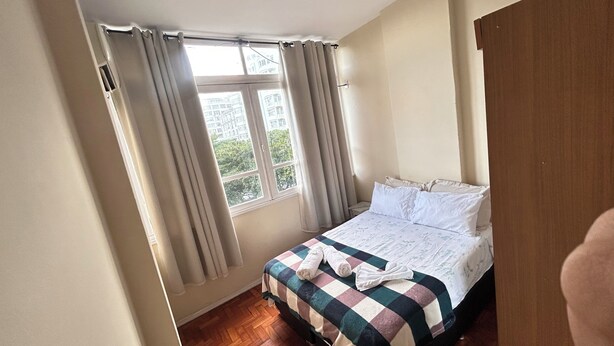 Un dormitorio con cama, cortinas, ventana y suelo de madera.