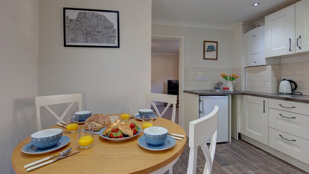 Un coin repas avec une table ronde, des chaises, des aliments pour le petit-déjeuner et une œuvre d’art représentant un paysage urbain accrochée au mur.