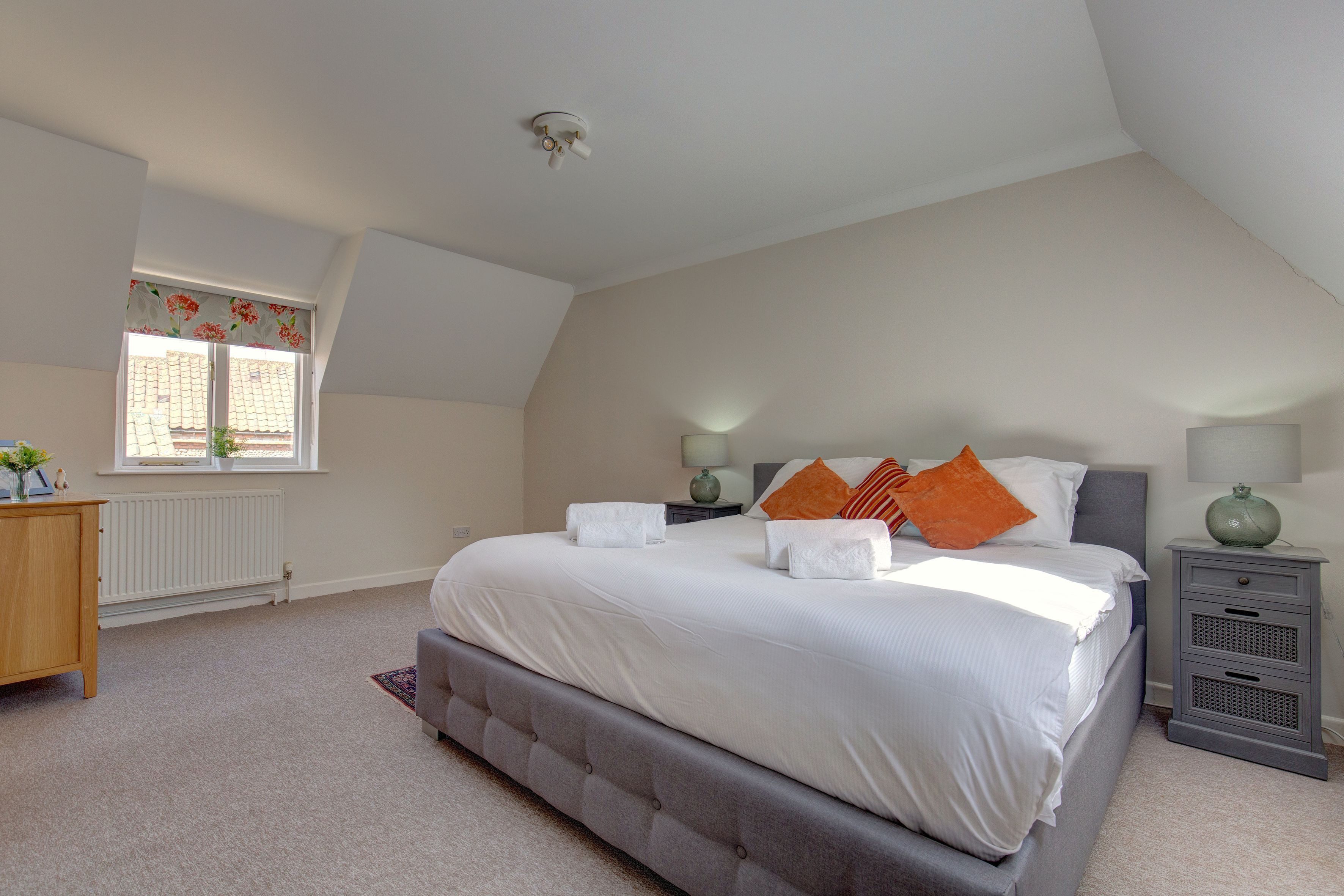 A bedroom with a large bed, a nightstand, a dresser, a window with curtains, and a radiator.