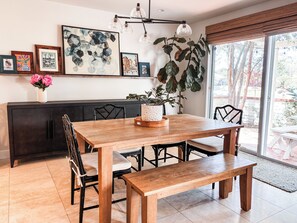 Uma área de refeições com mesa de madeira, cadeiras, um banco, planta em vaso e quadros nas paredes.