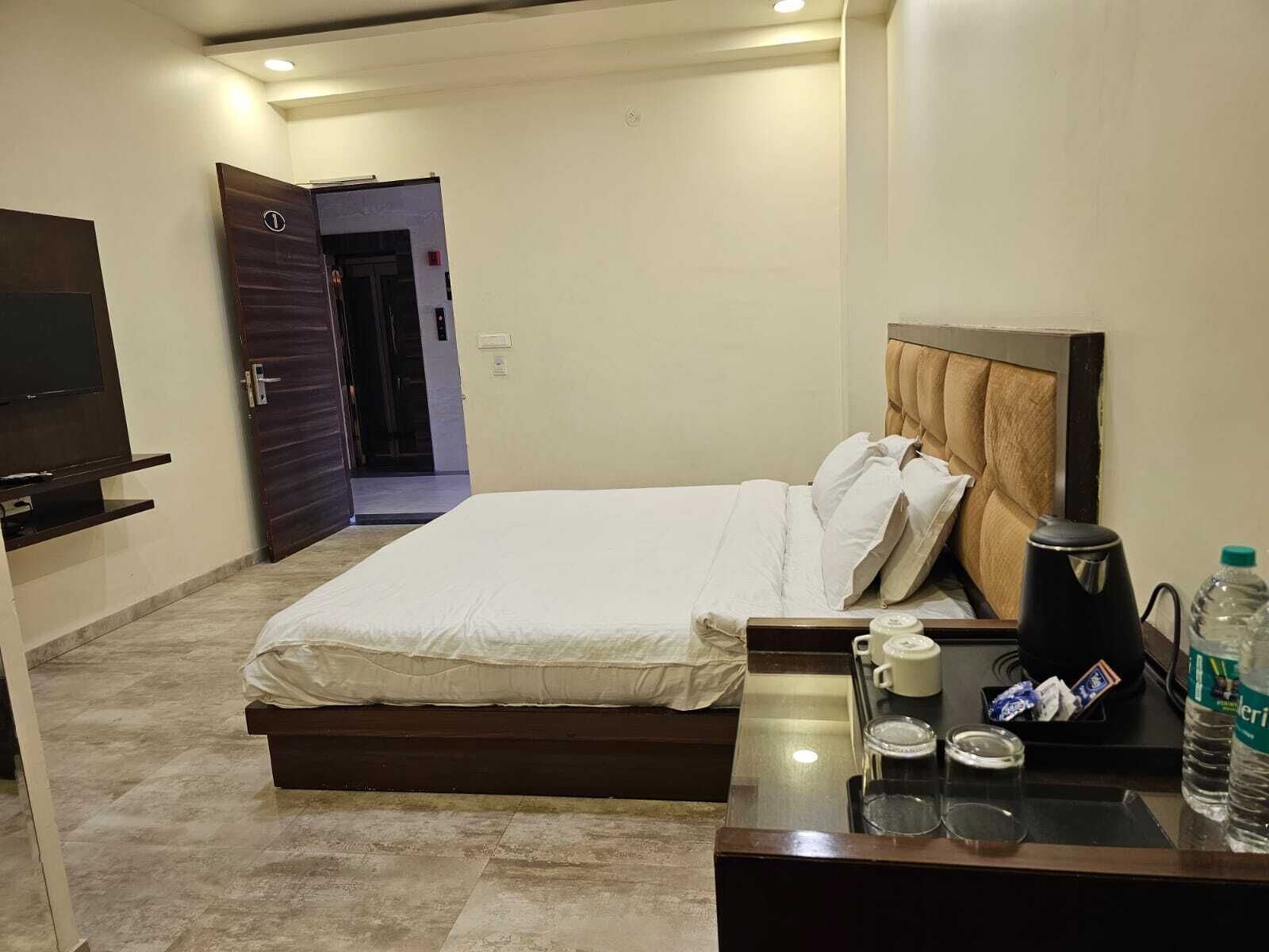 A hotel room with a bed, bedside table, TV, and a door leading to another room.