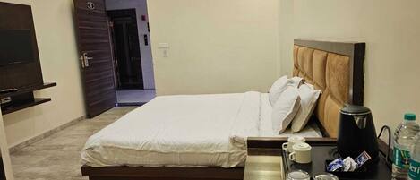 A hotel room with a bed, bedside table, TV, and a door leading to another room.