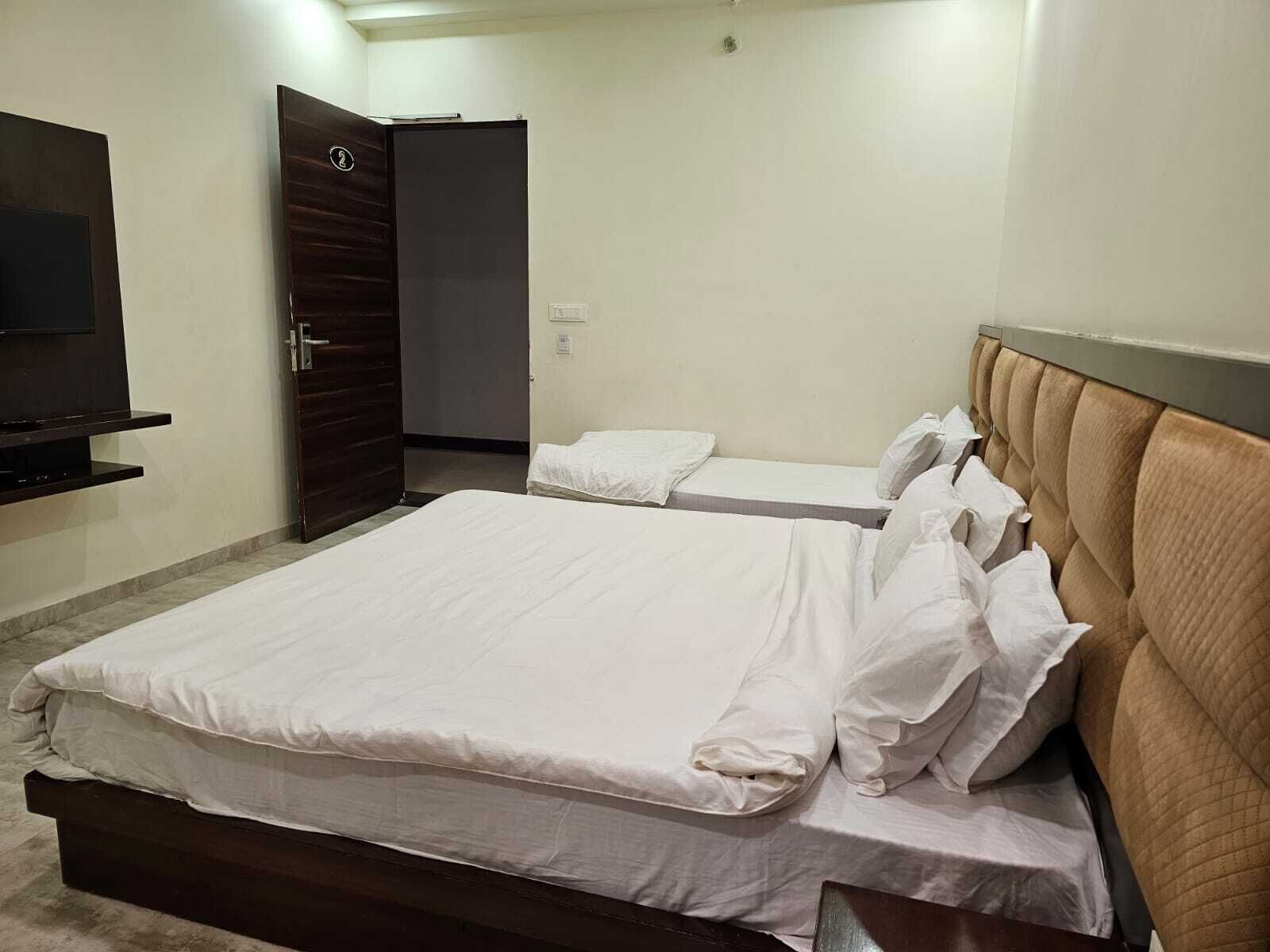 Hotelkamer met een groot bed, een kleiner bed, een aan de muur bevestigde televisie en een deur met een nummerbord.
