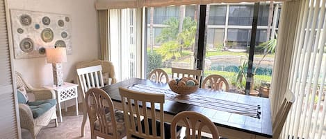 A dining area with a table, chairs, a lamp, and a view of the outdoors.