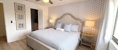 A bedroom with a bed, a ceiling fan, a nightstand, a lamp, and a window with curtains.