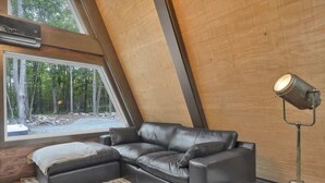 A modern interior with a black leather sofa, a standing floor lamp, and a large window offering a view of a forest.