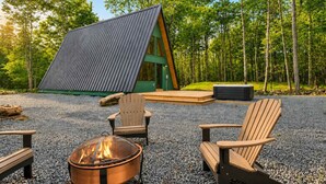 A modern cabin with a sloped roof, a fire pit, and outdoor seating.