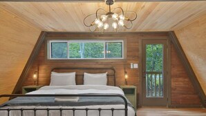A bedroom with a sloped ceiling, a bed, a chandelier, a window, and a door.