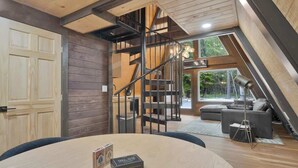 A loft-style room with a wooden ceiling, a spiral staircase, a large window, and a sofa.