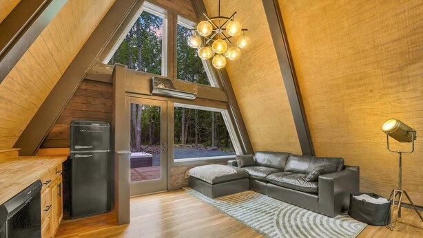 A modern loft bedroom with a large skylight, a black refrigerator, a leather sofa, and a floor lamp.