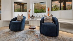 Een kamer met twee blauwe fauteuils, een klein bijzettafeltje en uitzicht op een canyon door grote ramen.