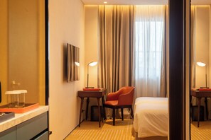 A hotel room with a bed, a chair, a desk, a mirror, and curtains.