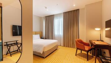A hotel room with a bed, a desk, a chair, a TV, and a large window with curtains.