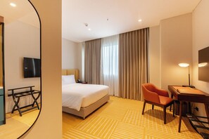 A hotel room with a bed, a desk, a chair, a TV, and a large window with curtains.