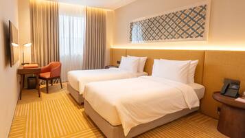 A hotel room with two beds, a desk with a chair, a telephone, and a wall-mounted artwork.