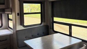 Ein kompaktes Wohnmobil-Interieur mit Esstisch, Sitzbank, kleiner Küchenzeile und Fenster mit Blick ins Freie.