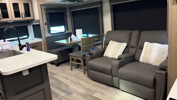 Ein kompaktes Wohnmobil-Interieur mit einer Küchenzeile, einer Sitzecke mit Fernsessel und einem kleinen Tisch.