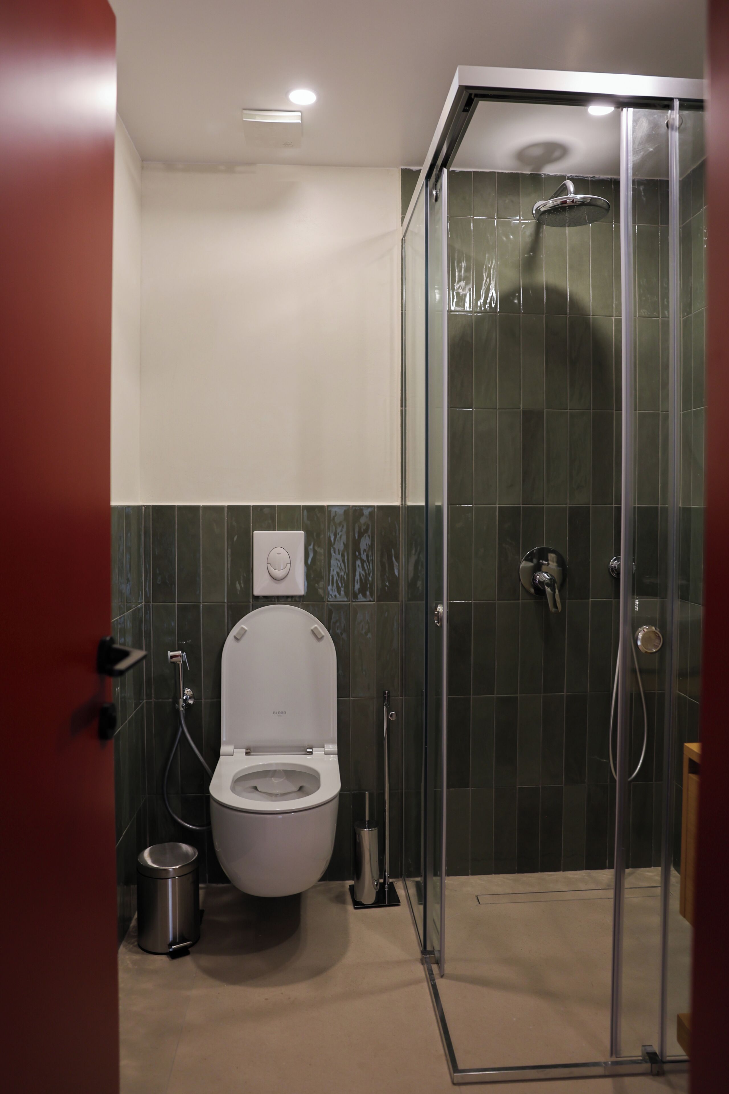 A modern bathroom with a toilet, a shower enclosure, and a trash bin.