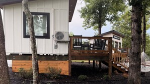 A cabin with a deck, surrounded by trees and mulch.