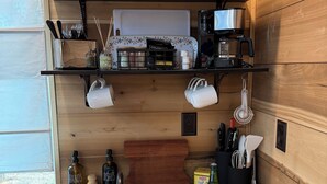 A kitchen with wooden walls, a white countertop, a sink, and various kitchen items like a coffee maker, utensils, and a watermelon slice.